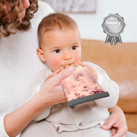 A baby wearing a cream knit outfit is being fed from a clear silicone pouch with a dark gray silicone spout, held by an adult in a cream sweater. A '2023 bounty' award badge is visible in the top right corner.