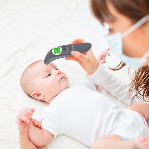 Baby being measured with a digital thermometer by a person wearing a face mask.