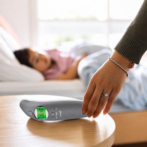 Person using a digital thermometer on a surface with a blurred background of a person lying down.
