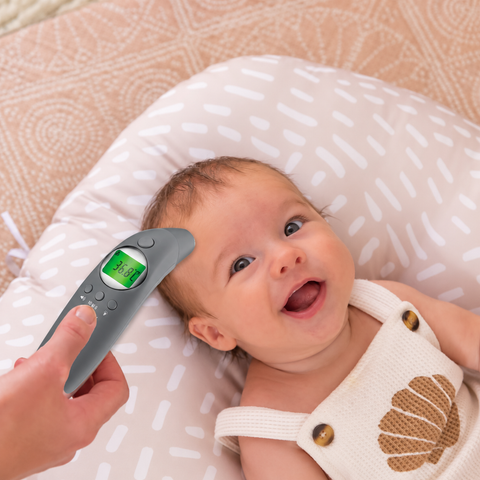 Baby lying on a white pillow with a digital thermometer held above its head.