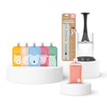 A set of cherub baby Pouches in yellow, peach, blue, pink, and mint green, displayed alongside a clear and black filling station on white display pedestals against a white background.